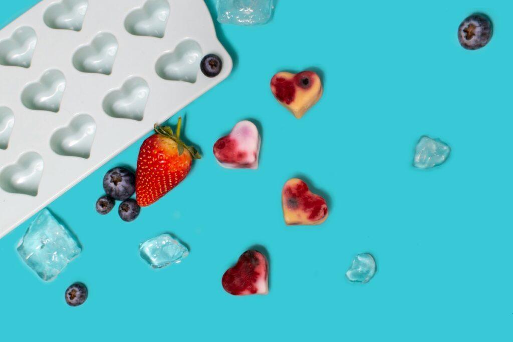 DIY frozen dog treats in heart-shaped molds with fruit and ice cubes